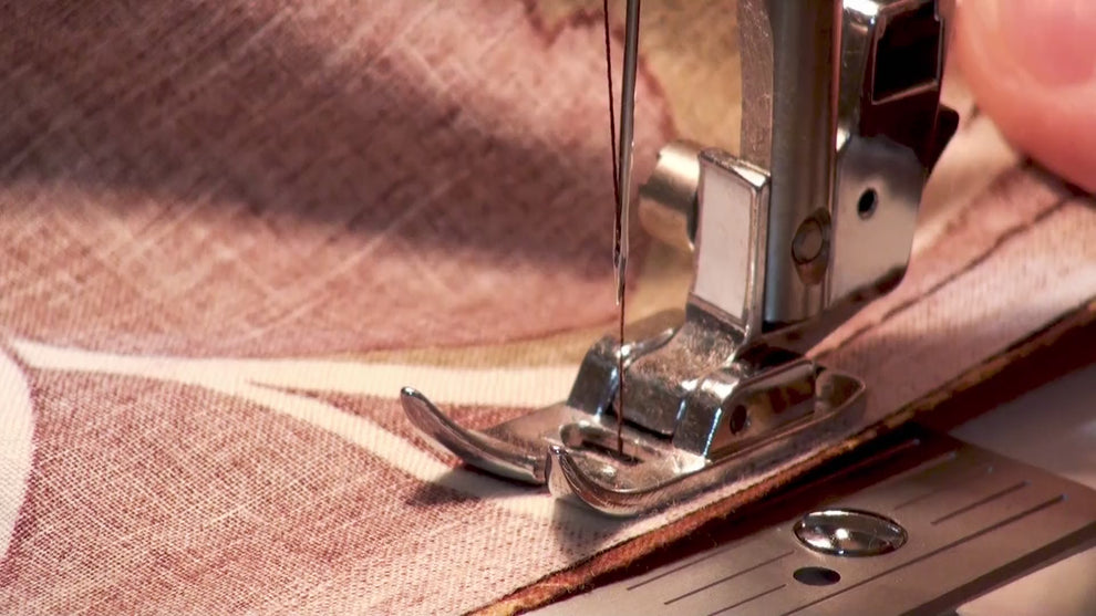 Hands guiding plain cream fabric under a sewing machine needle.